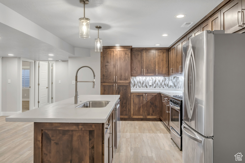 Kitchen featuring appliances with stainless steel finishes, light wood-style flooring, a kitchen island with sink, decorative light fixtures, and recessed lighting