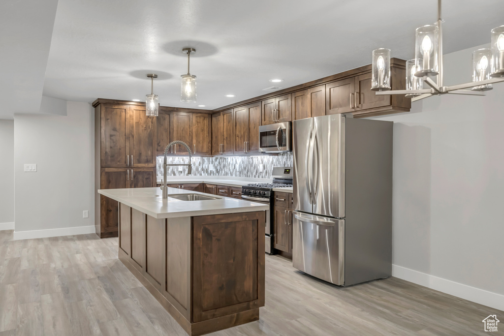 Kitchen featuring appliances with stainless steel finishes, light wood-style floors, light countertops, a center island with sink, and pendant lighting