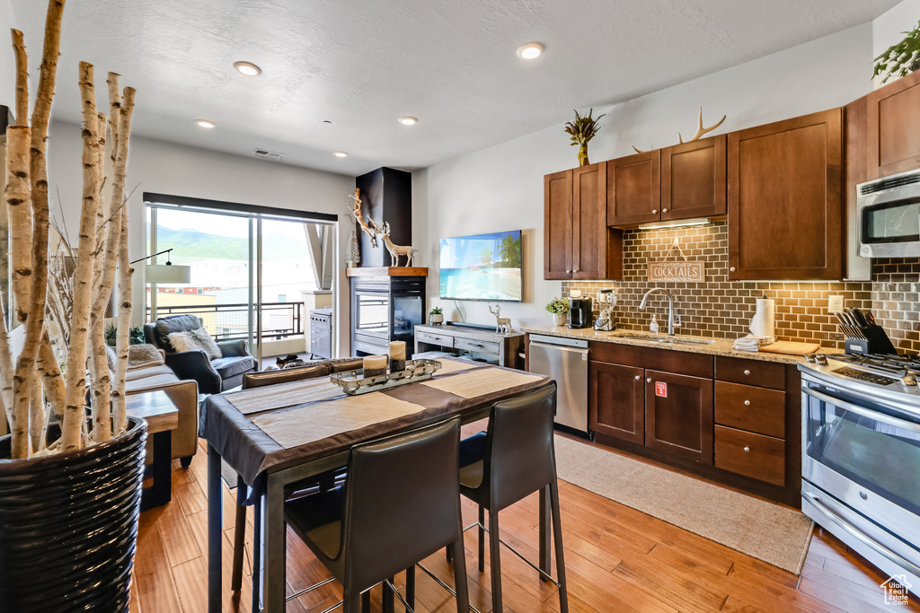 Kitchen with stainless steel appliances, backsplash, light wood-type flooring, light stone countertops, and recessed lighting