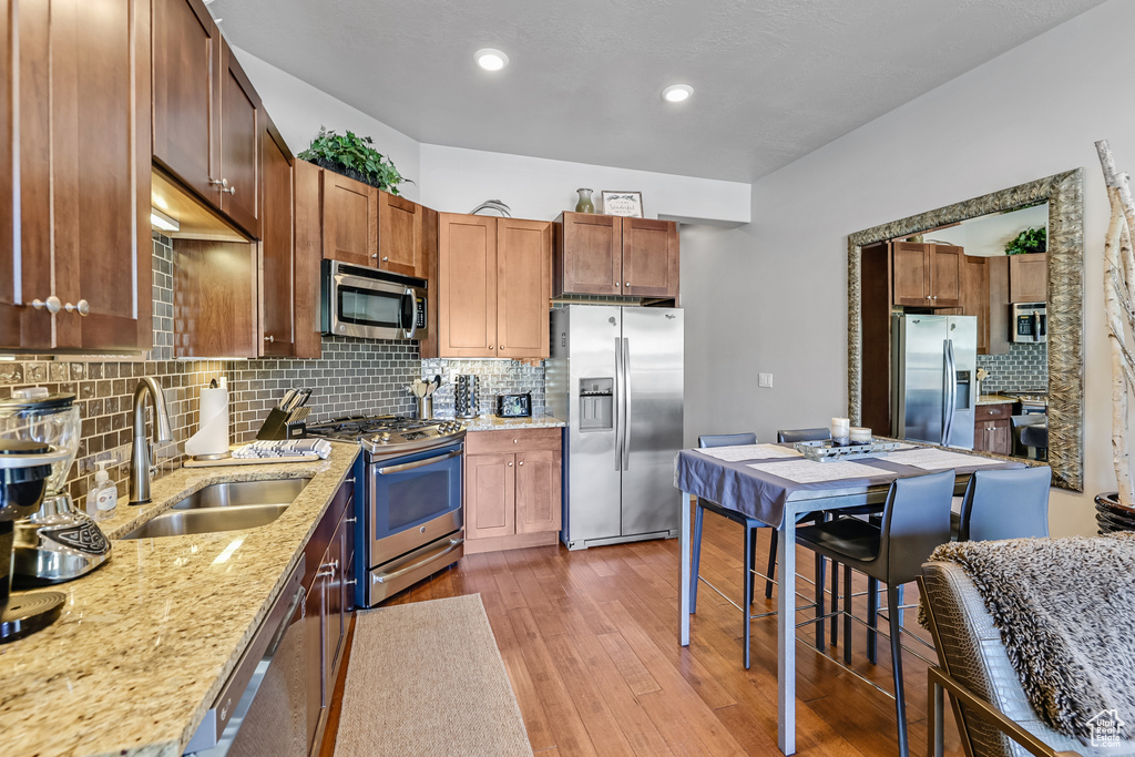 Kitchen featuring stainless steel appliances, decorative backsplash, wood finished floors, light stone counters, and recessed lighting