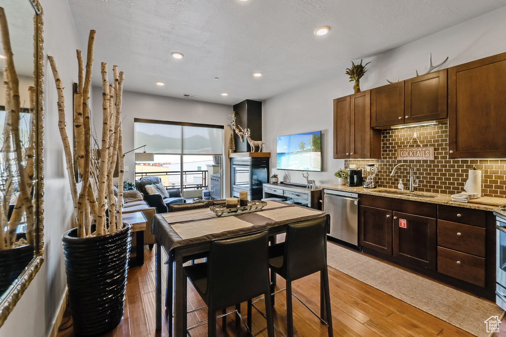 Kitchen featuring dishwasher, light wood finished floors, backsplash, light stone countertops, and dark brown cabinets