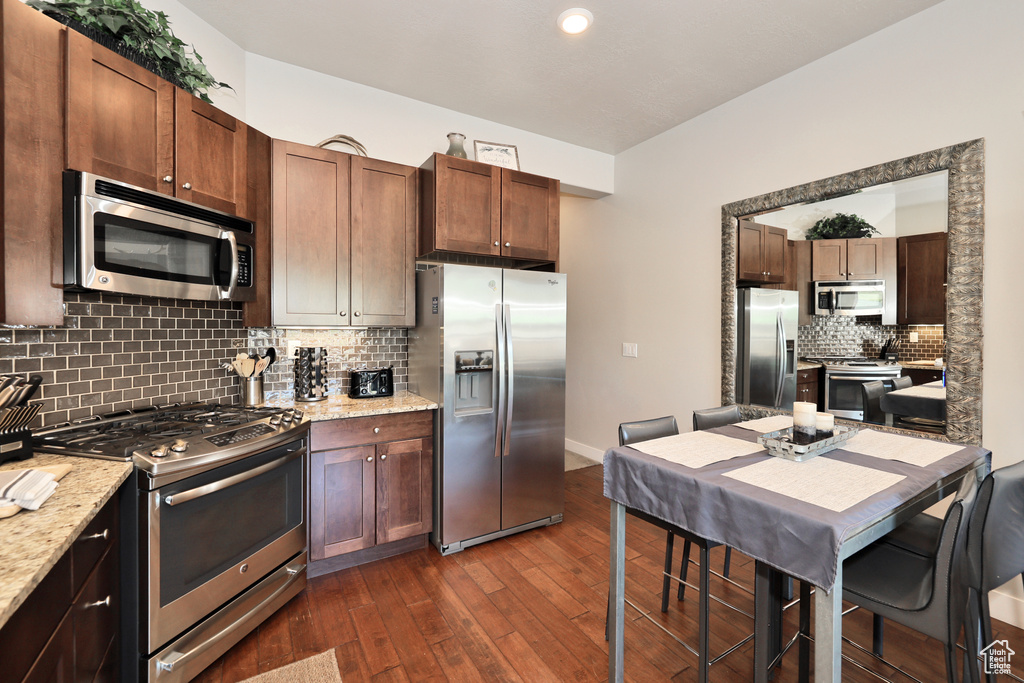 Kitchen with stainless steel appliances, dark wood finished floors, tasteful backsplash, and light stone countertops
