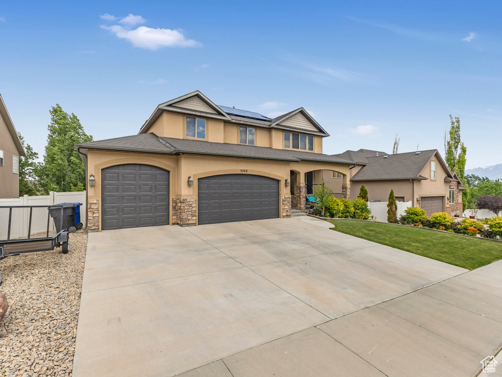 View of front of house featuring stucco siding, stone siding, driveway, roof mounted solar panels, and a garage