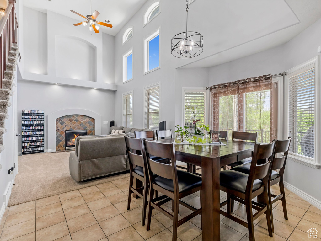 Dining room with light tile patterned floors, a tile fireplace, light colored carpet, a ceiling fan, and a high ceiling