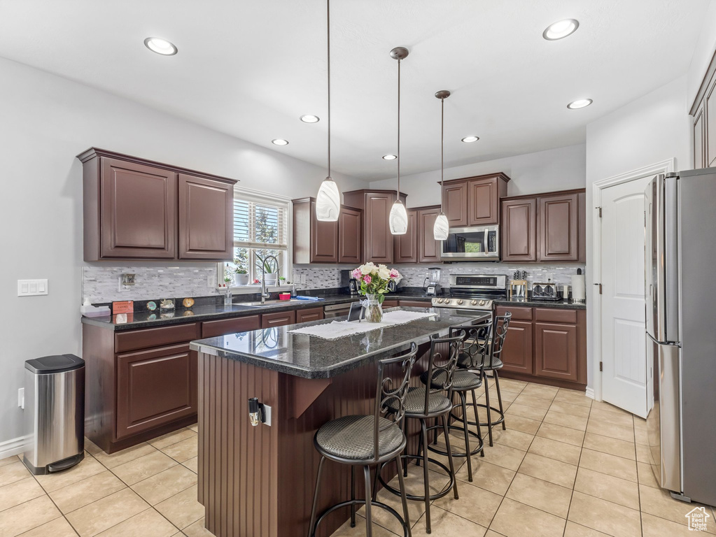 Kitchen featuring appliances with stainless steel finishes, light tile patterned floors, tasteful backsplash, a kitchen breakfast bar, and a kitchen island