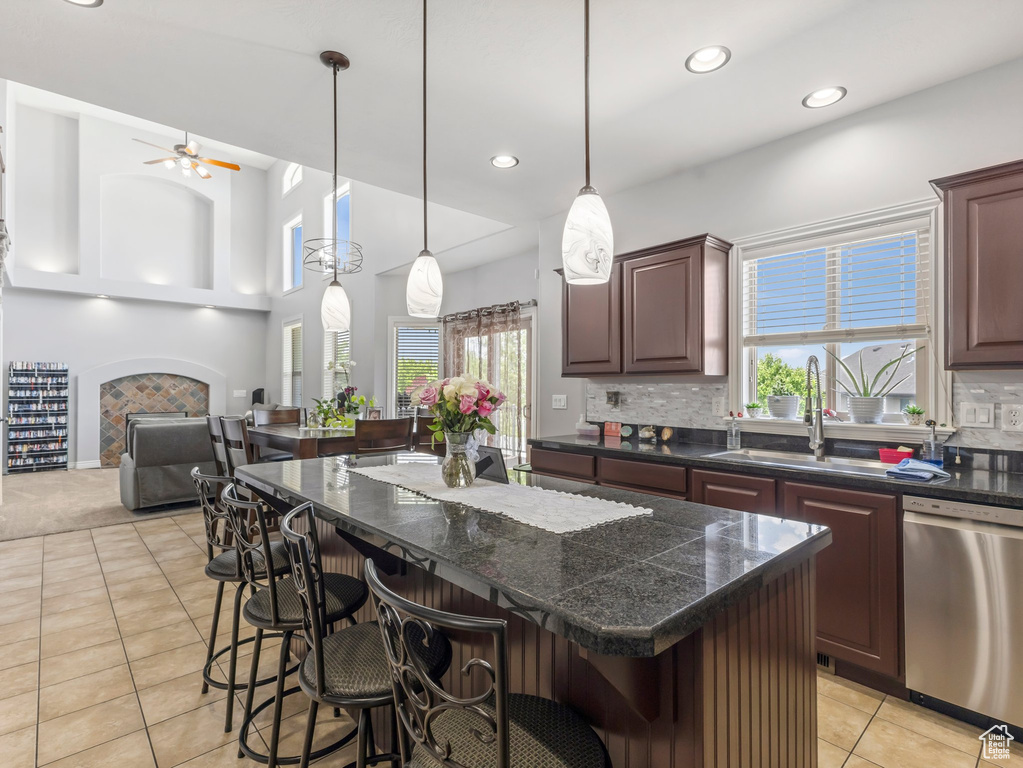 Kitchen featuring stainless steel dishwasher, ceiling fan, a kitchen island, light tile patterned floors, and a breakfast bar area