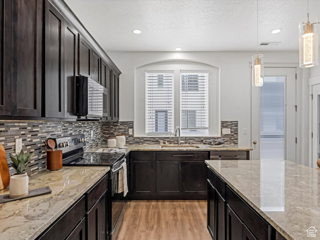 Kitchen featuring appliances with stainless steel finishes, light wood-style floors, decorative backsplash, hanging light fixtures, and recessed lighting