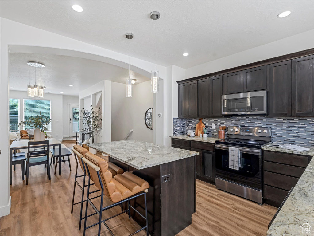 Kitchen featuring appliances with stainless steel finishes, tasteful backsplash, light wood-type flooring, light stone counters, and a center island