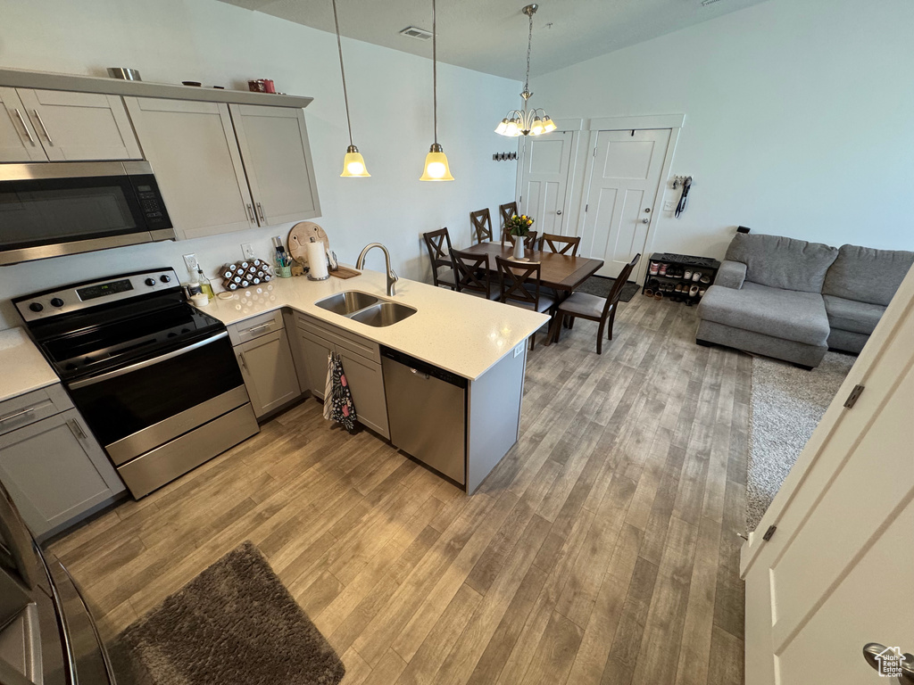 Kitchen featuring stainless steel appliances, a peninsula, a chandelier, light wood-style flooring, and light countertops