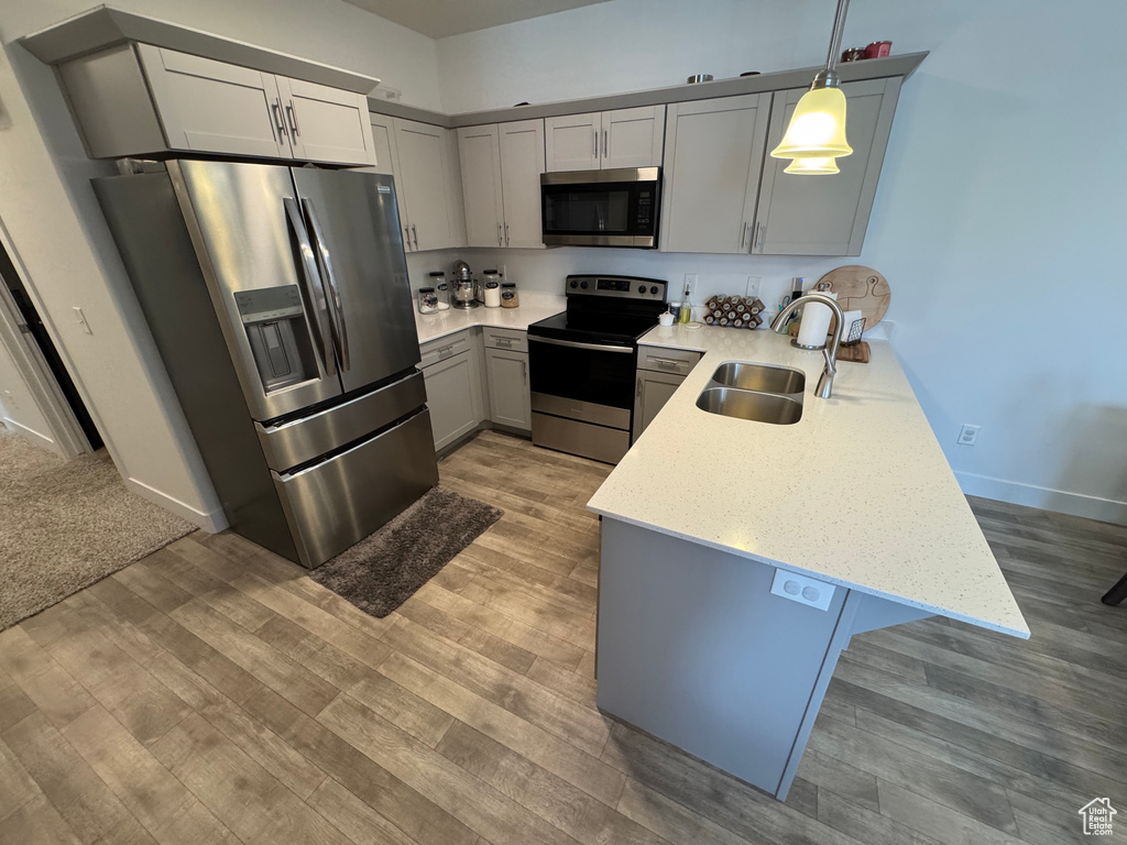 Kitchen featuring appliances with stainless steel finishes, a peninsula, gray cabinetry, light wood-style flooring, and pendant lighting