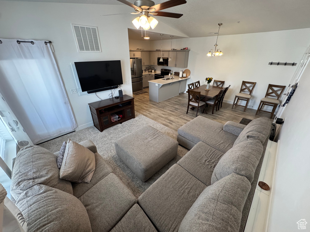 Living room with lofted ceiling, ceiling fan, a chandelier, and light wood-style floors