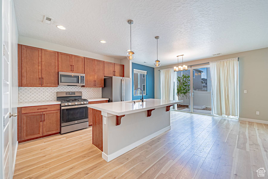 Kitchen featuring appliances with stainless steel finishes, light countertops, brown cabinets, light wood-style floors, and backsplash