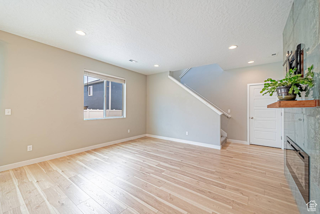 Unfurnished living room with stairway, light wood-style flooring, a textured ceiling, and recessed lighting
