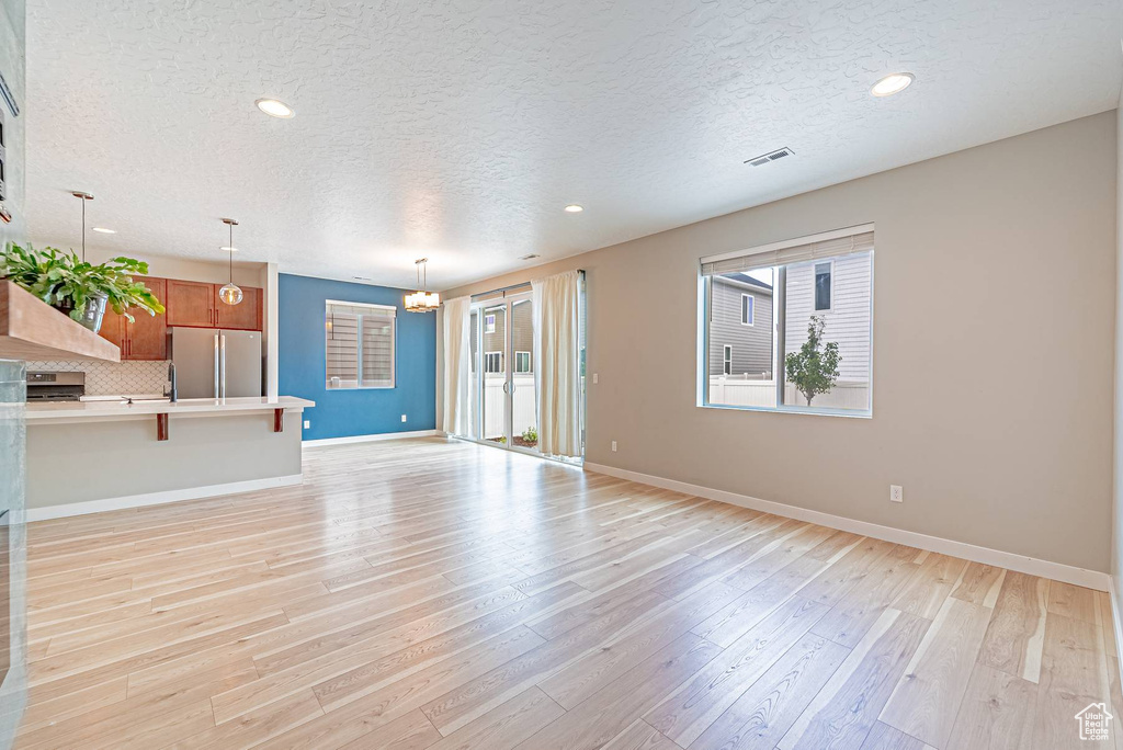 Unfurnished living room featuring a textured ceiling, a chandelier, light wood finished floors, and recessed lighting