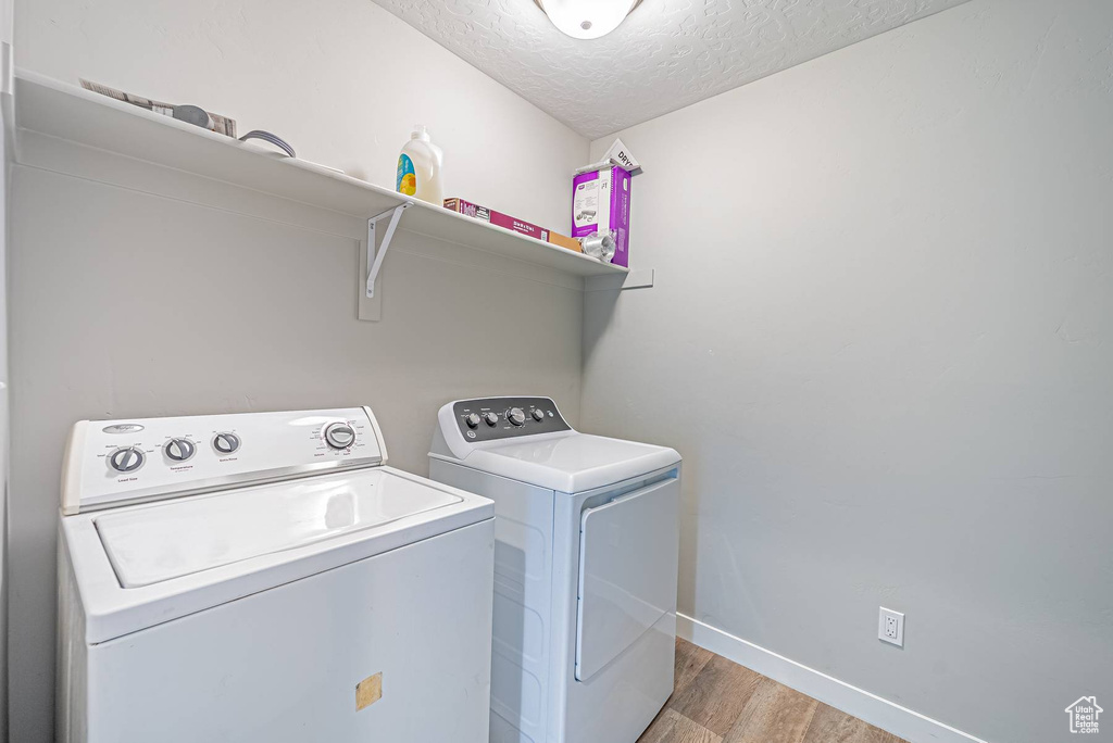 Laundry room with light wood-style floors, washer and dryer, and a textured ceiling