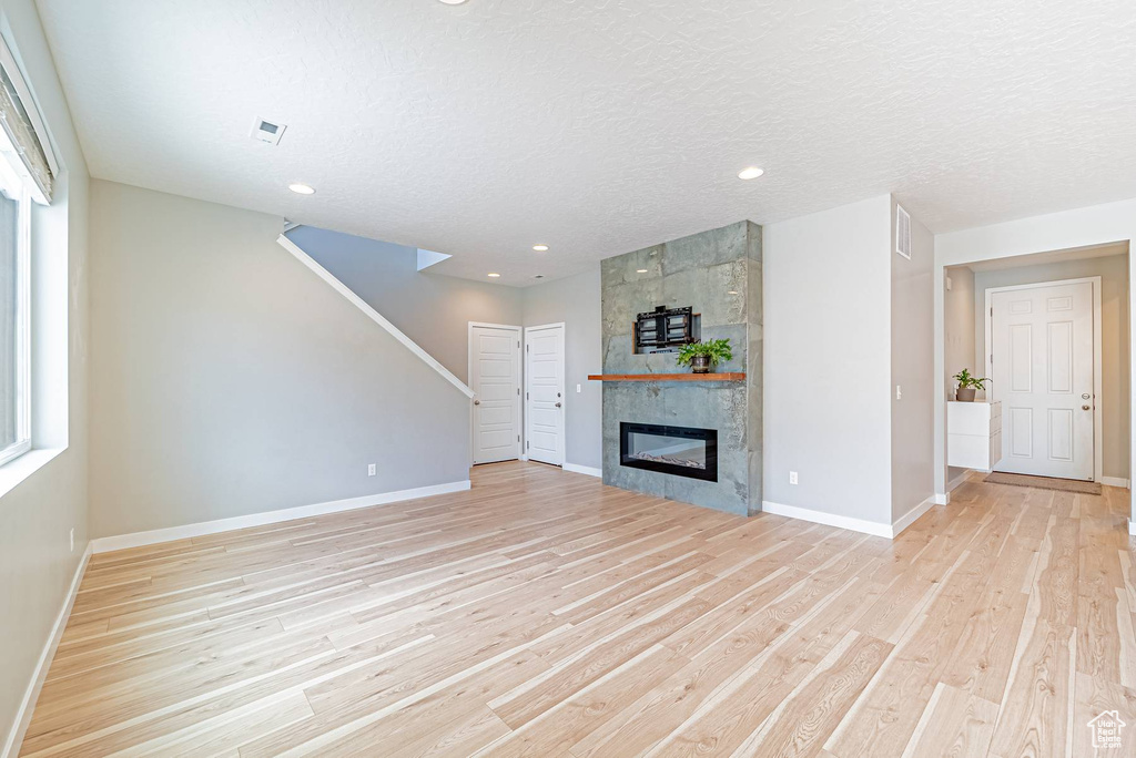 Unfurnished living room with light wood finished floors, stairway, a large fireplace, plenty of natural light, and recessed lighting