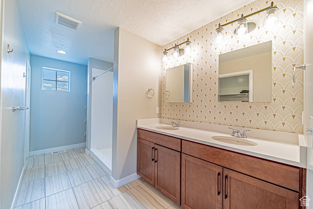 Full bath with double vanity, a textured ceiling, and a shower