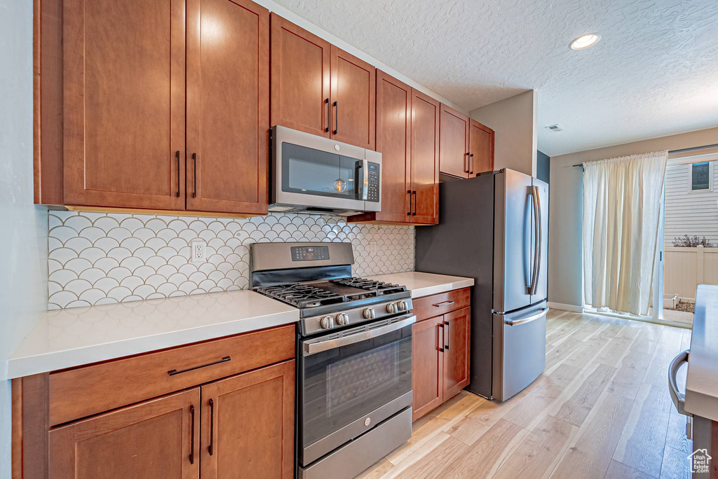 Kitchen featuring stainless steel appliances, light wood-type flooring, a textured ceiling, light countertops, and decorative backsplash