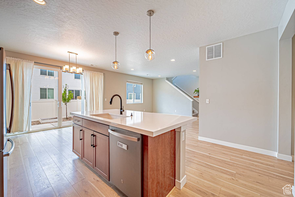 Kitchen featuring stainless steel appliances, a textured ceiling, a chandelier, light wood-style floors, and hanging light fixtures
