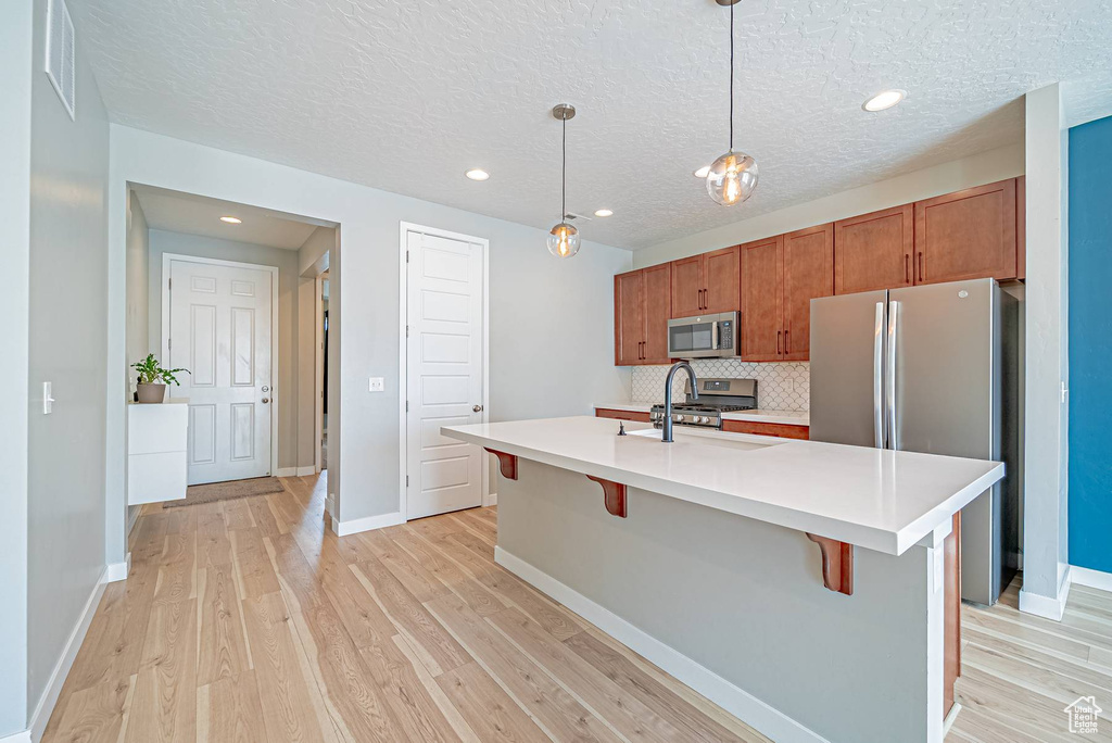Kitchen featuring stainless steel appliances, brown cabinets, light wood-style flooring, light countertops, and a kitchen bar
