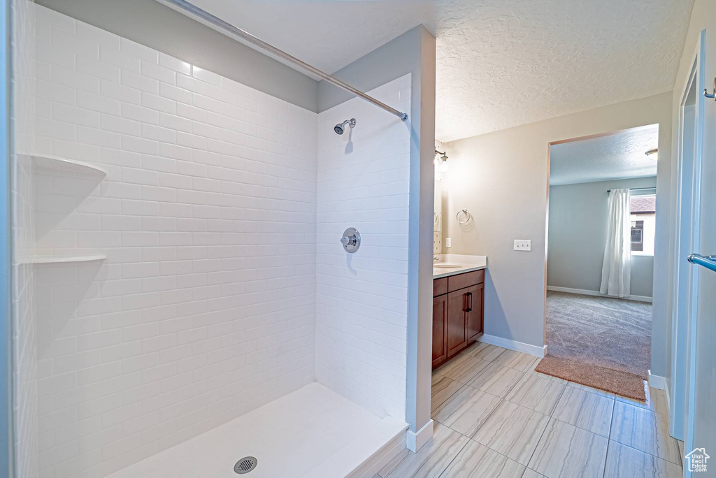 Full bathroom featuring vanity, tiled shower, tile patterned flooring, and a textured ceiling