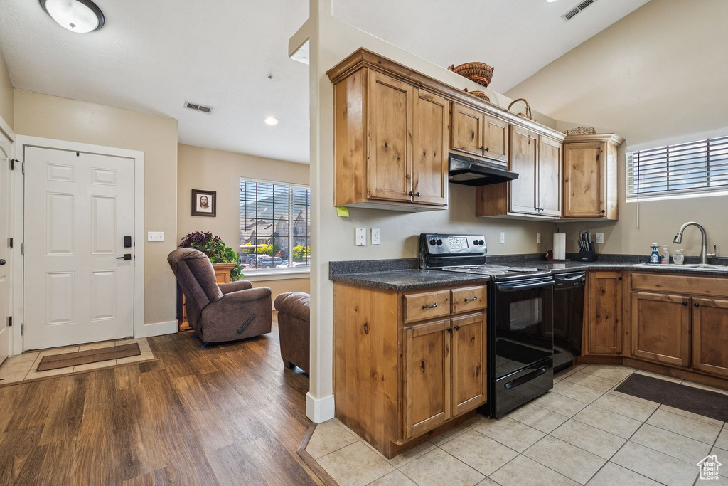 Kitchen with black appliances, under cabinet range hood, dark countertops, light wood-type flooring, and brown cabinetry