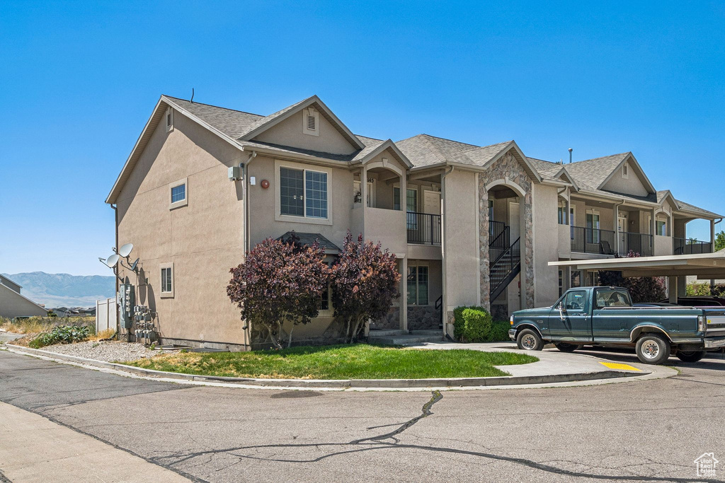 View of property with stucco siding, covered parking, stairway, and a mountain view