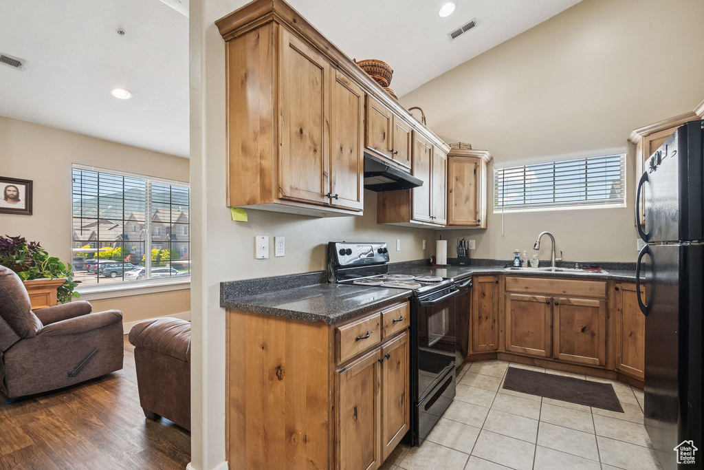 Kitchen with black appliances, under cabinet range hood, brown cabinetry, vaulted ceiling, and recessed lighting