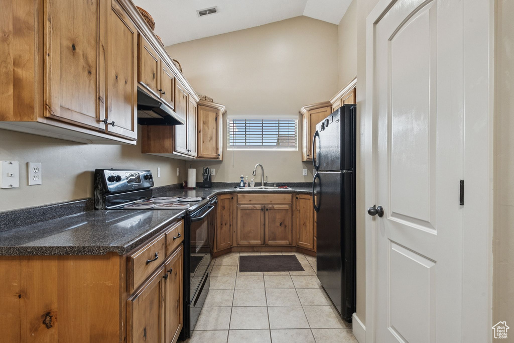 Kitchen with black appliances, under cabinet range hood, brown cabinets, light tile patterned floors, and lofted ceiling