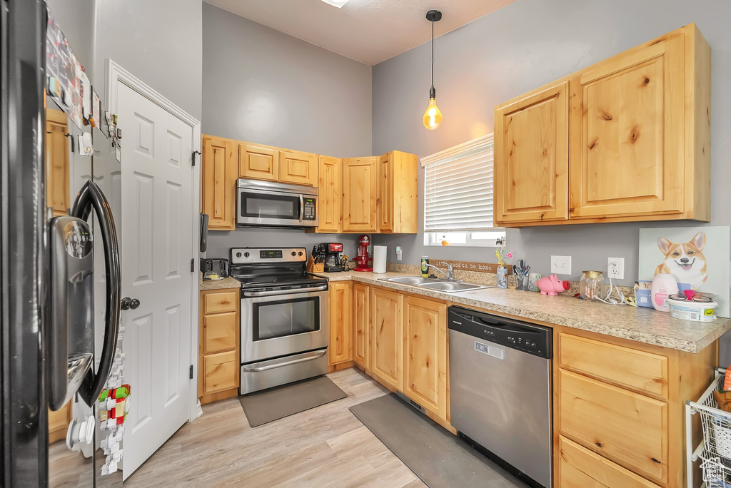 Kitchen featuring appliances with stainless steel finishes, light brown cabinets, light wood finished floors, light countertops, and a high ceiling