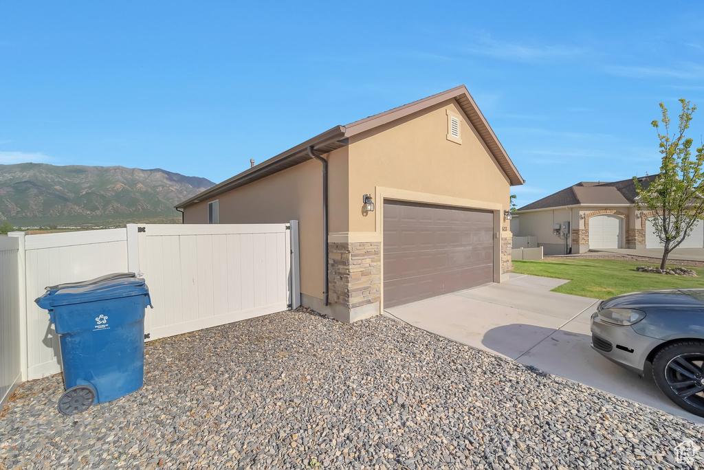 View of side of property featuring a mountain view, stone siding, concrete driveway, stucco siding, and a garage