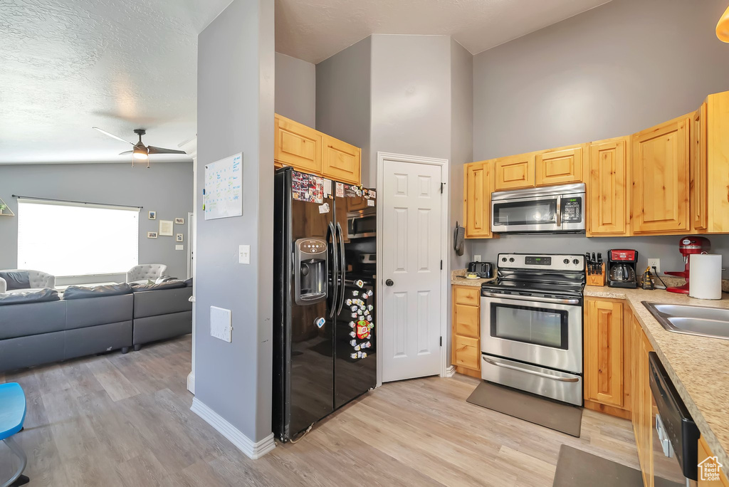 Kitchen with stainless steel appliances, open floor plan, light brown cabinets, light wood-style floors, and light countertops