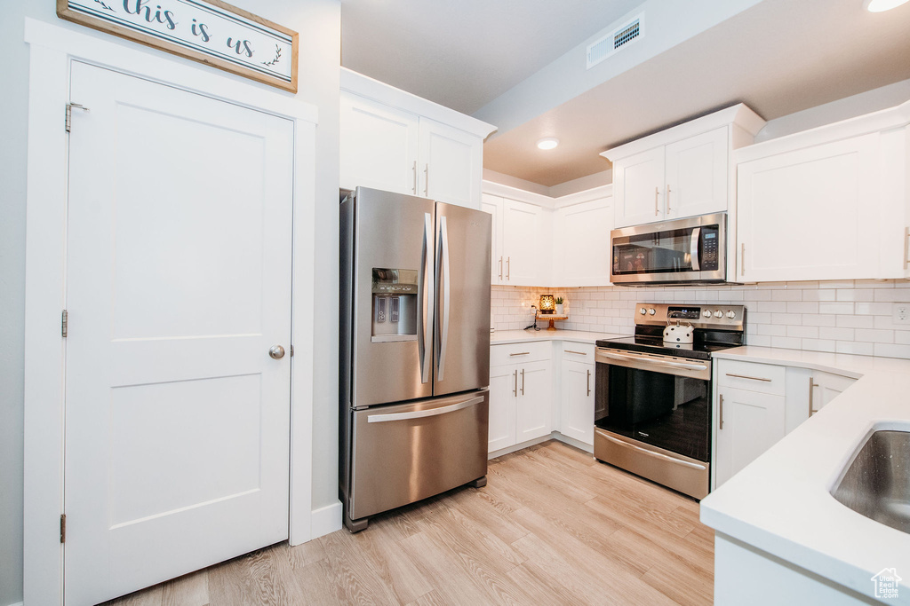 Kitchen with appliances with stainless steel finishes, light wood-style flooring, light countertops, white cabinetry, and recessed lighting