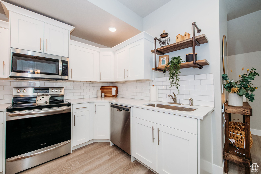 Kitchen featuring stainless steel appliances, open shelves, light wood-style floors, light countertops, and recessed lighting