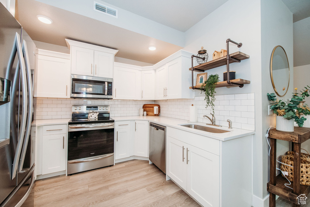 Kitchen featuring stainless steel appliances, light countertops, white cabinets, light wood-type flooring, and backsplash