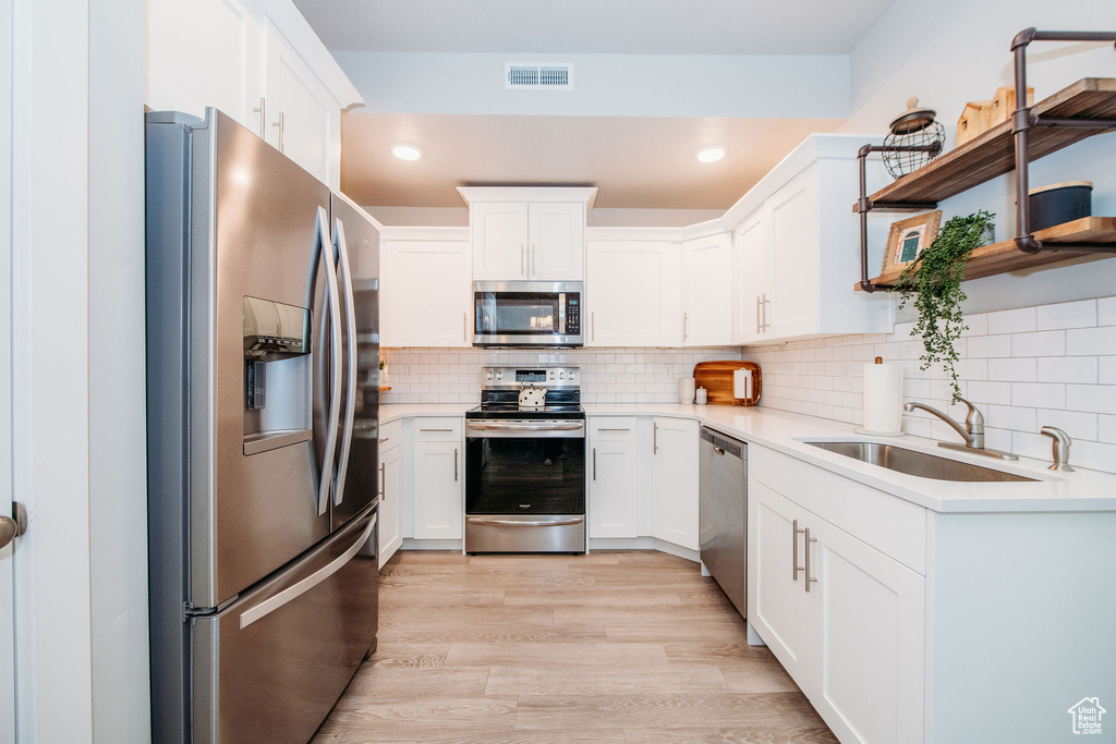 Kitchen featuring stainless steel appliances, white cabinets, light countertops, open shelves, and decorative backsplash
