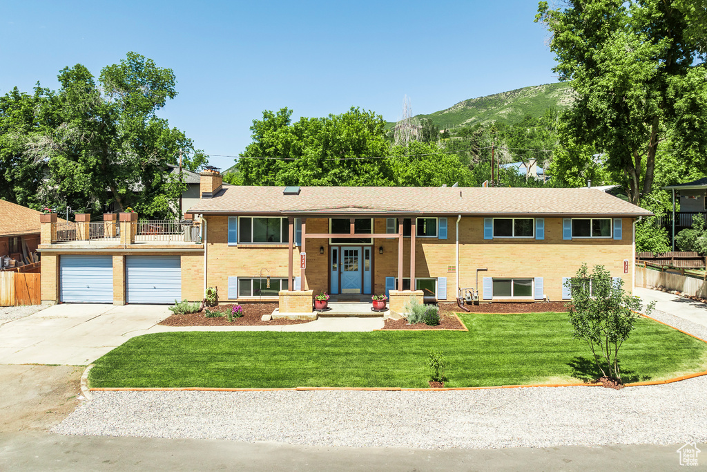 Split foyer home with concrete driveway, a mountain view, a chimney, and a balcony