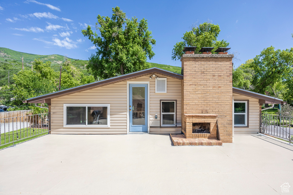 Back of property with an outdoor brick fireplace, a patio area, a chimney, and a mountain view