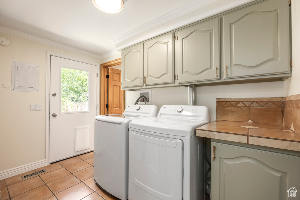 Washroom featuring cabinet space, washer and dryer, light tile patterned floors, electric panel, and crown molding