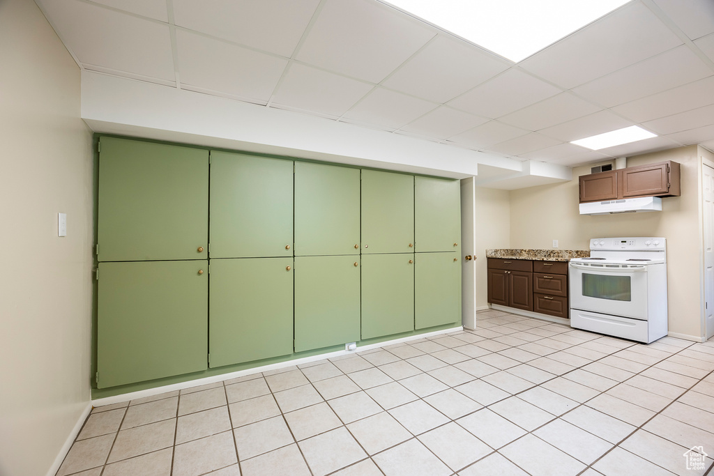 Kitchen featuring white electric range, under cabinet range hood, a drop ceiling, light tile patterned floors, and green cabinets