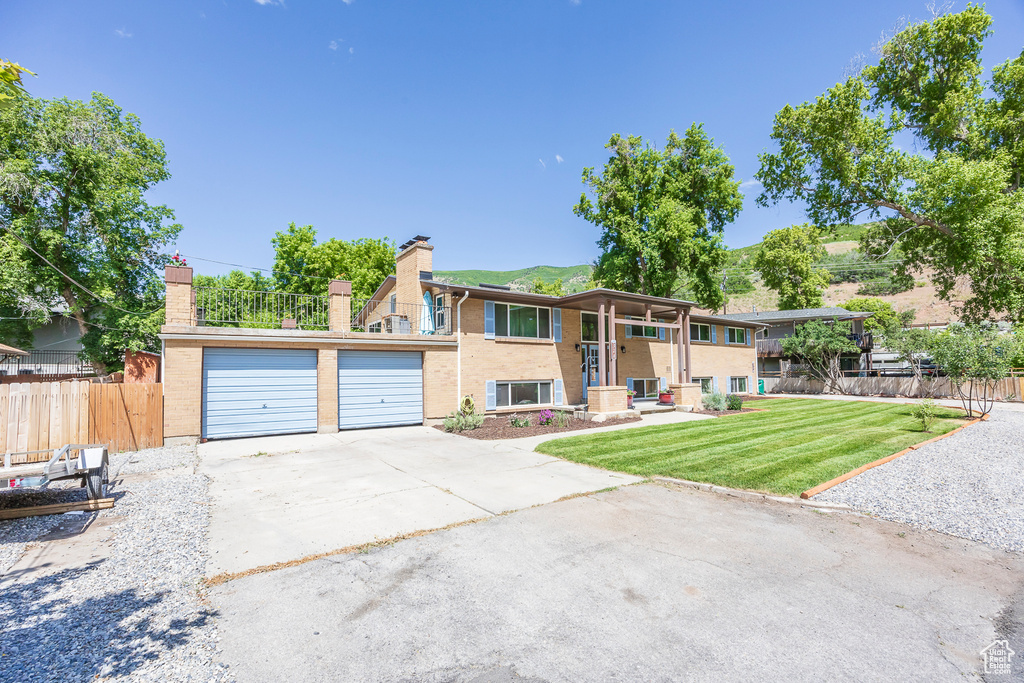 Raised ranch with a chimney, brick siding, a garage, and concrete driveway