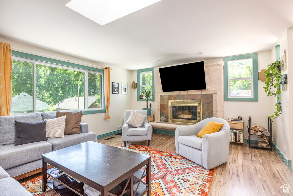 Living room with a tiled fireplace, light wood-type flooring, and a skylight
