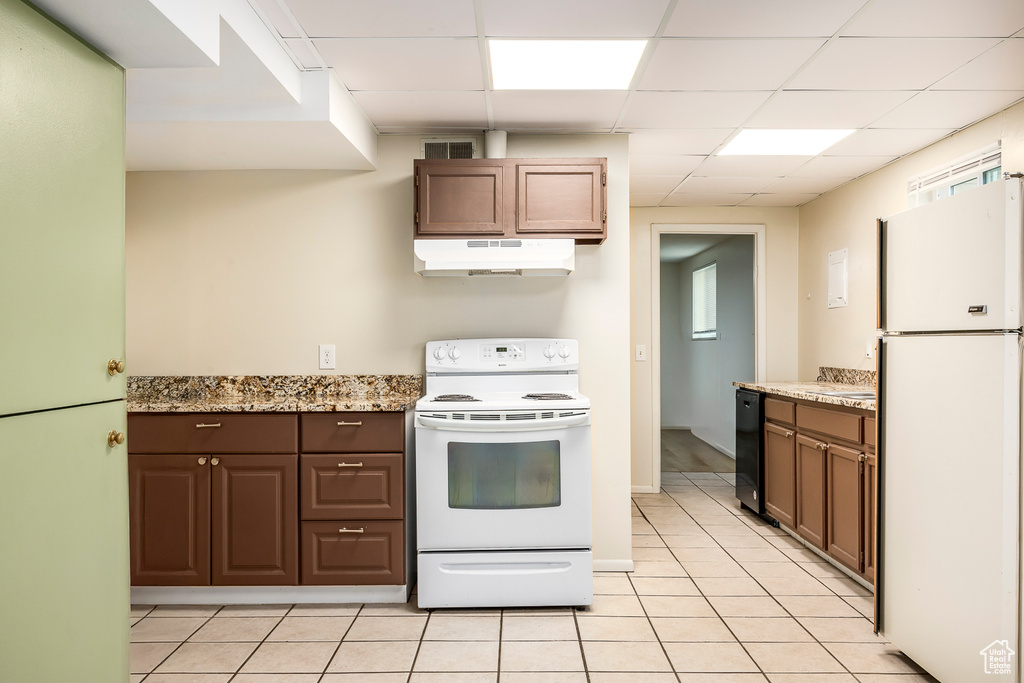 Kitchen featuring white appliances, under cabinet range hood, a paneled ceiling, light tile patterned floors, and light stone countertops