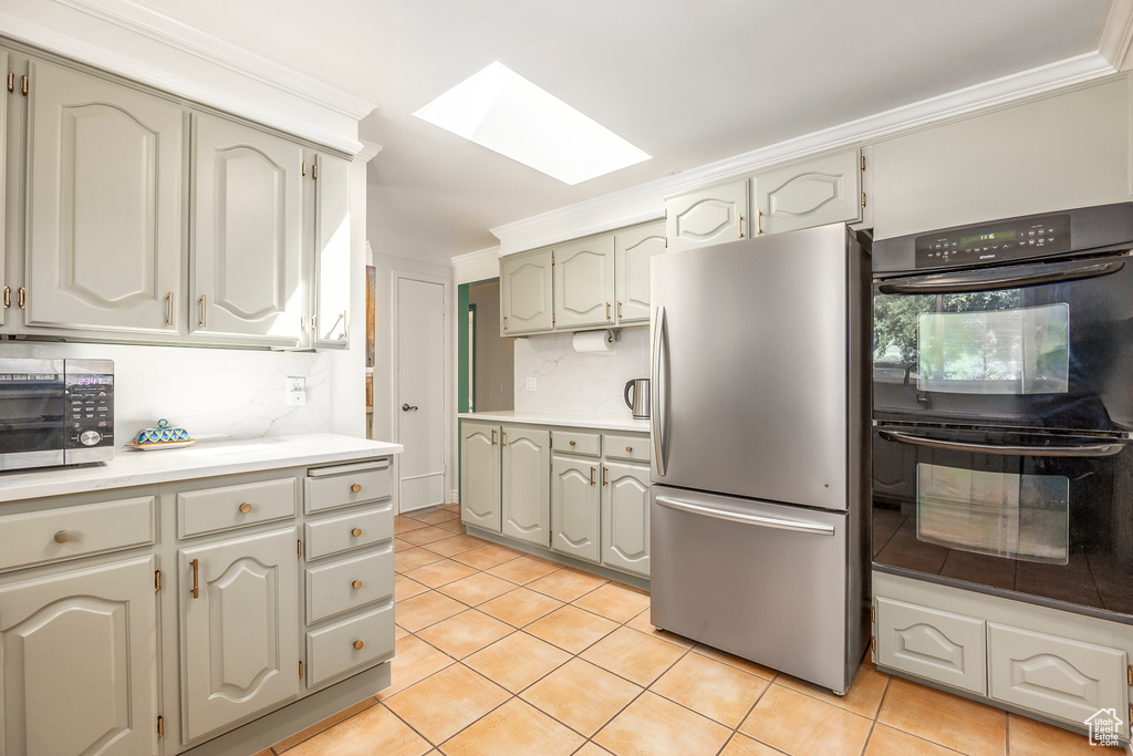 Kitchen with appliances with stainless steel finishes, a skylight, light tile patterned floors, light countertops, and ornamental molding
