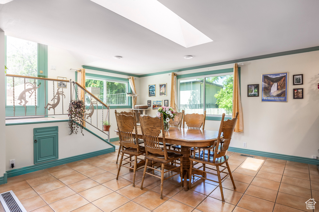 Dining space featuring a skylight, light tile patterned floors, crown molding, and stairway