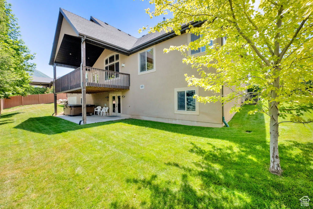 Back of house featuring a hot tub, a patio, and stucco siding