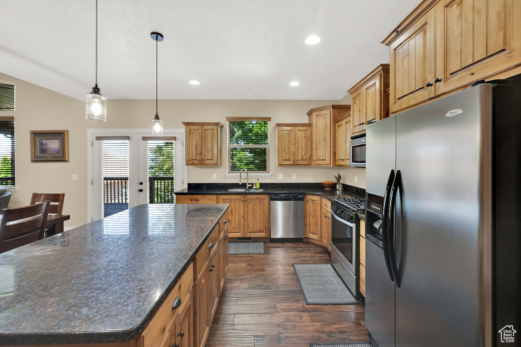 Kitchen with appliances with stainless steel finishes, dark wood-style flooring, a kitchen island, recessed lighting, and pendant lighting