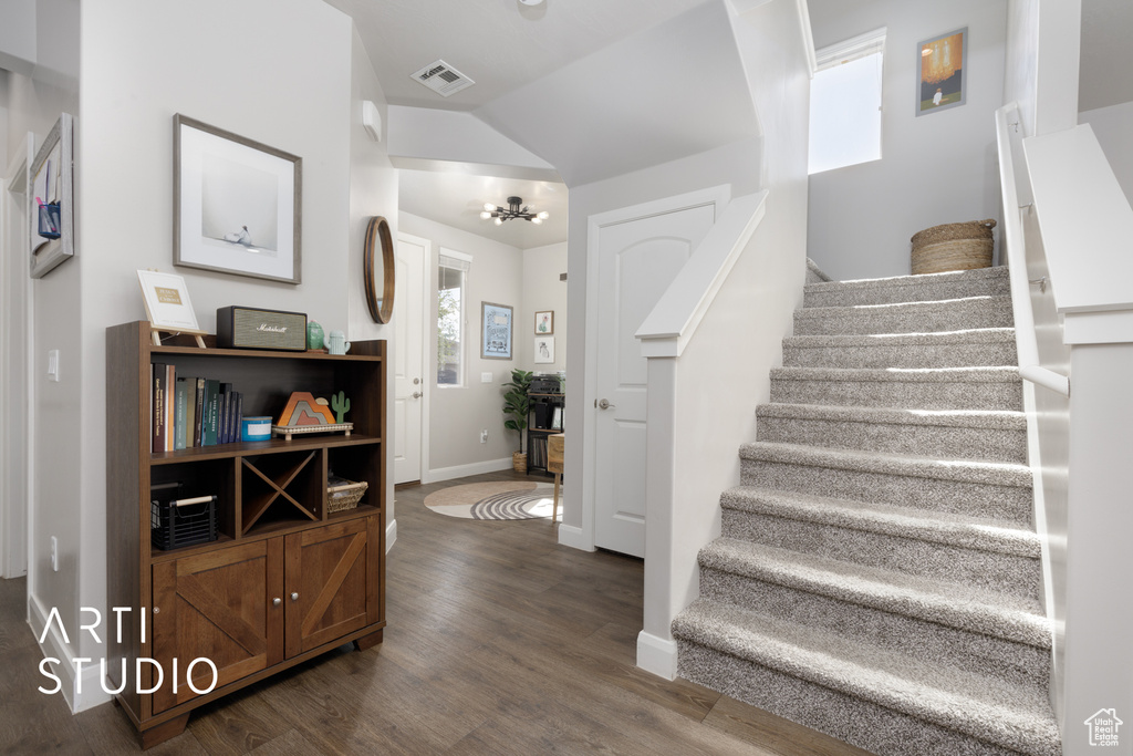 Stairway with wood finished floors, lofted ceiling, and a chandelier