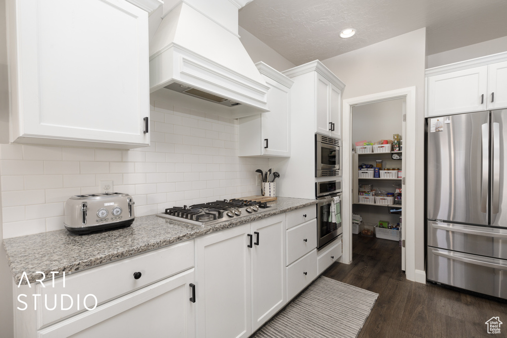 Kitchen with appliances with stainless steel finishes, custom exhaust hood, white cabinetry, and dark wood-style floors