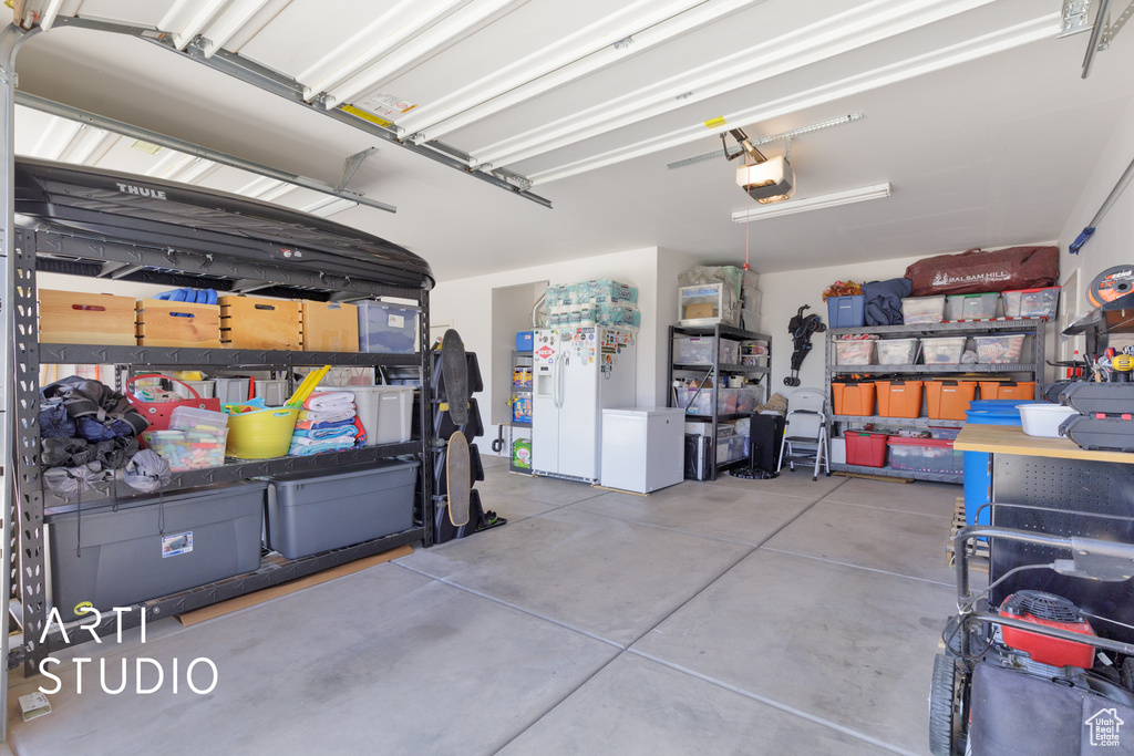 Garage with a garage door opener and white refrigerator with ice dispenser